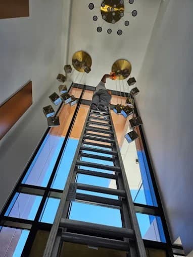 High-reach fixture cleaning from an extension ladder in a tall atrium