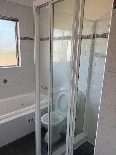 Bathroom with bathtub, glass shower and open toilet after cleaning