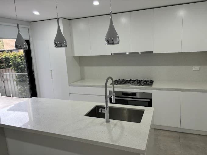 Modern white kitchen island with sink, cooktop and pendant lights after cleaning